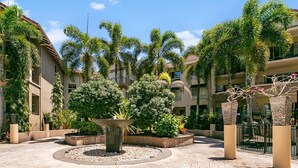 A courtyard with a central fountain, surrounded by palm trees and planters, with buildings in the background. - The Lakes Resort Cairns (Cairns North)