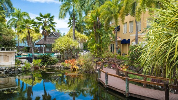 A tropical resort with a pool, palm trees, and a wooden bridge over a pond. - The Lakes Resort Cairns (Cairns North)