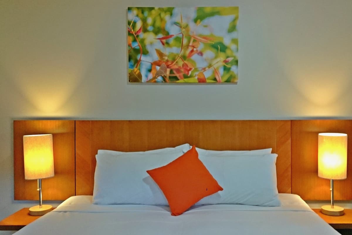 A neatly made bed with white and orange pillows, flanked by two bedside lamps on wooden nightstands.