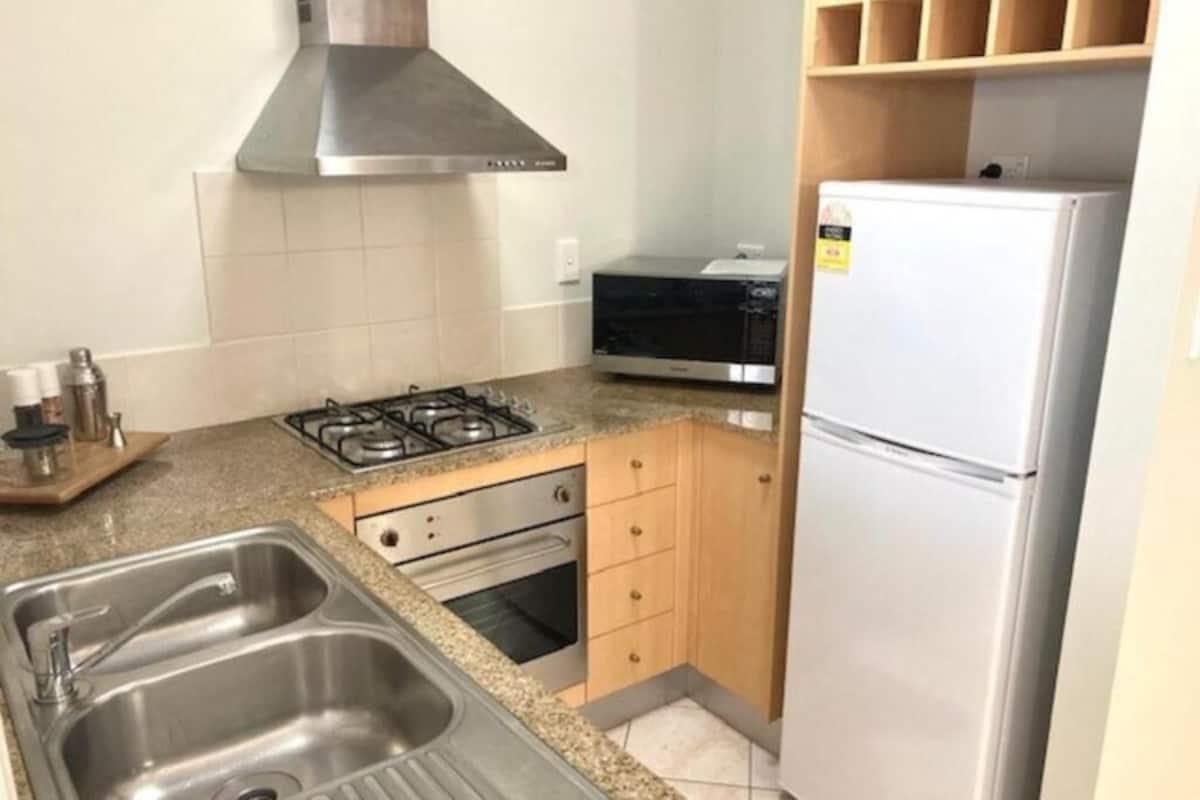 A compact kitchen with a gas stove, oven, stainless steel sink, and a white refrigerator.