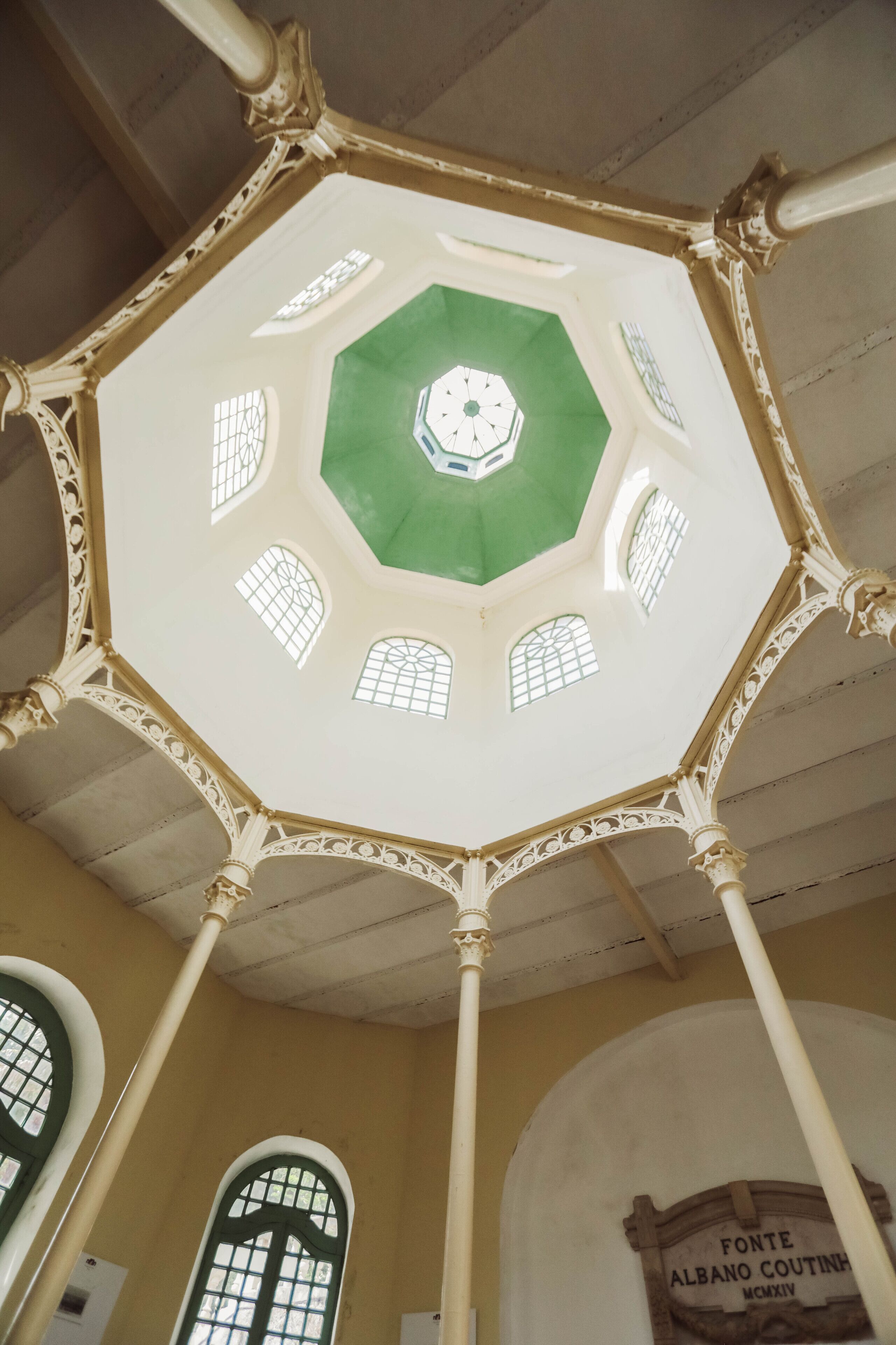 Un techo octogonal con detalles intrincados en blanco y oro, una cúpula central de vidrio verde y un cartel que dice 