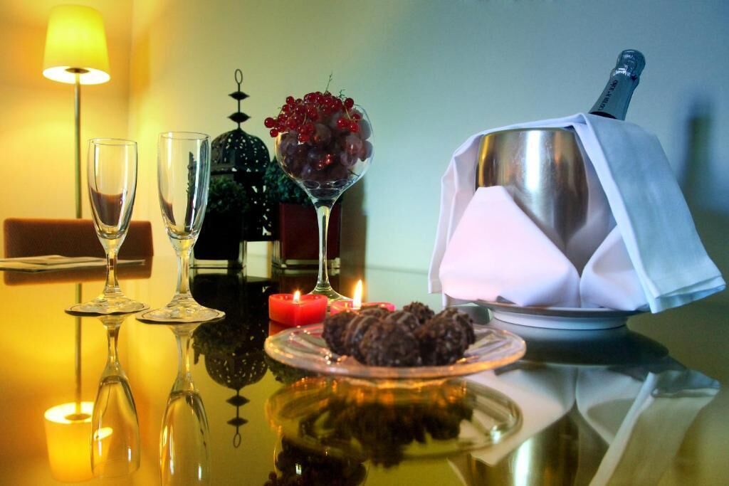 A table with two empty wine glasses, a glass of red grapes, a lit candle, and a chocolate dessert on a reflective surface.