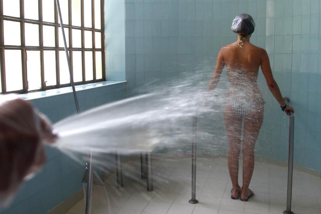 Una persona duchándose en un baño con ventana y paredes de azulejos.