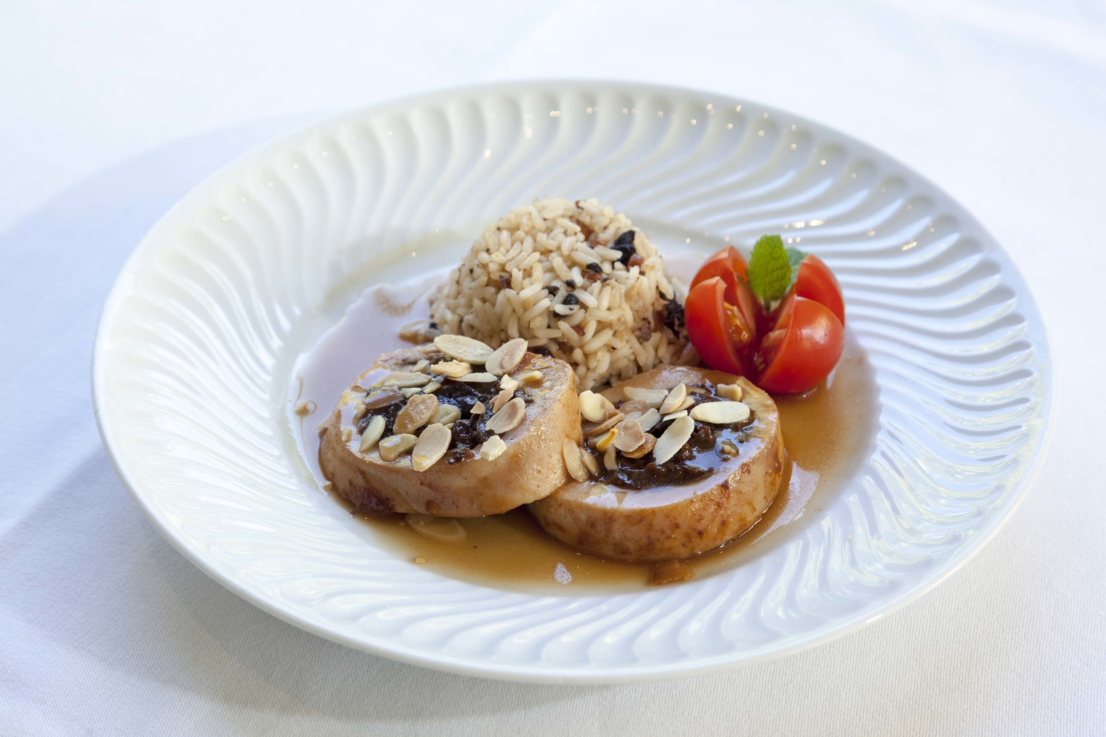 Une assiette contenant deux morceaux de viande, recouverts d’amandes, accompagnée d’une portion de riz et décorée de tomates cerises.