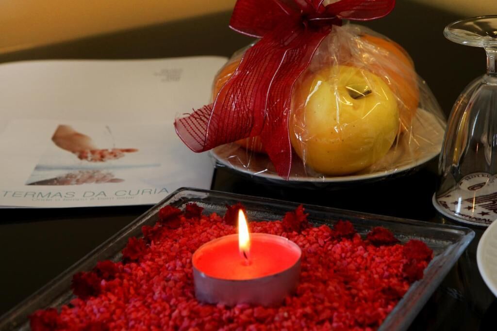 A candle on a tray with red petals, a plate with a wrapped fruit, and a menu.