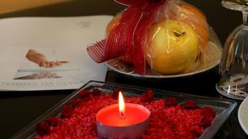 A candle on a tray with red petals, a plate with a wrapped fruit, and a menu.