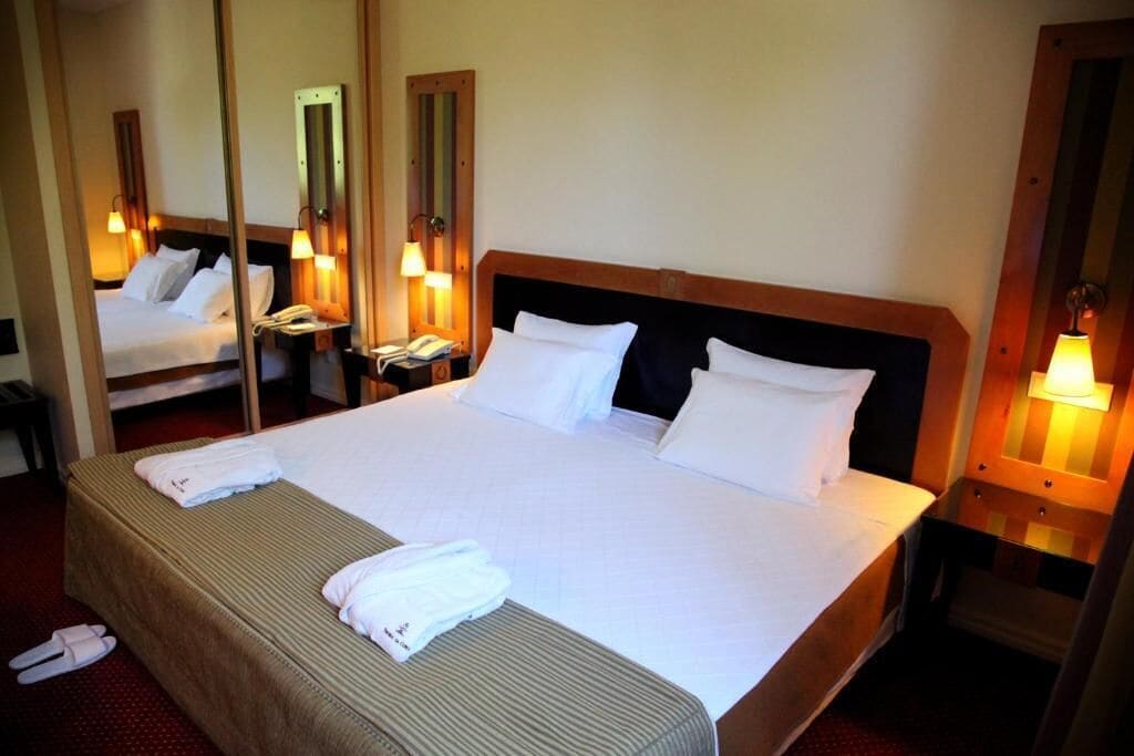 Une chambre d’hôtel avec un grand lit, deux tables de chevet, un miroir et une lampe fixée au mur.