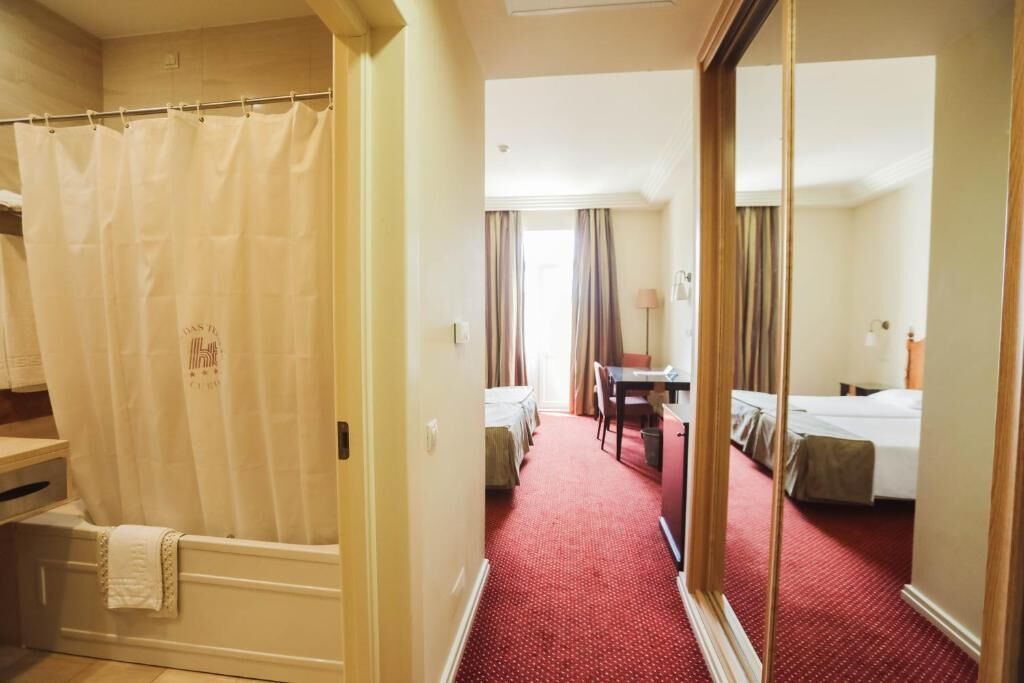 A hotel room with a red carpet, a shower curtain, a bed, a desk, and a mirror.