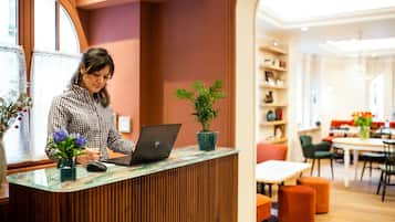 A reception desk with a laptop, a potted plant, and a vase with flowers.