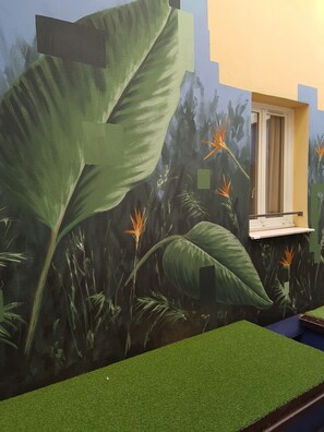 A room with a large mural of tropical foliage and a window with a white frame. - Hotel les Cigales (Nice)