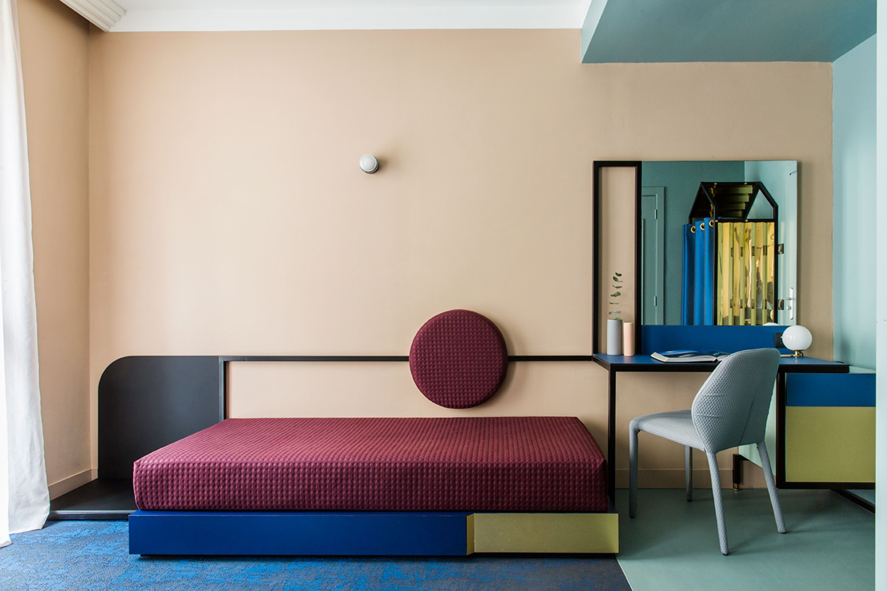 Una camera da letto con un letto, una scrivania, una sedia, uno specchio e un oggetto circolare fissato alla parete.