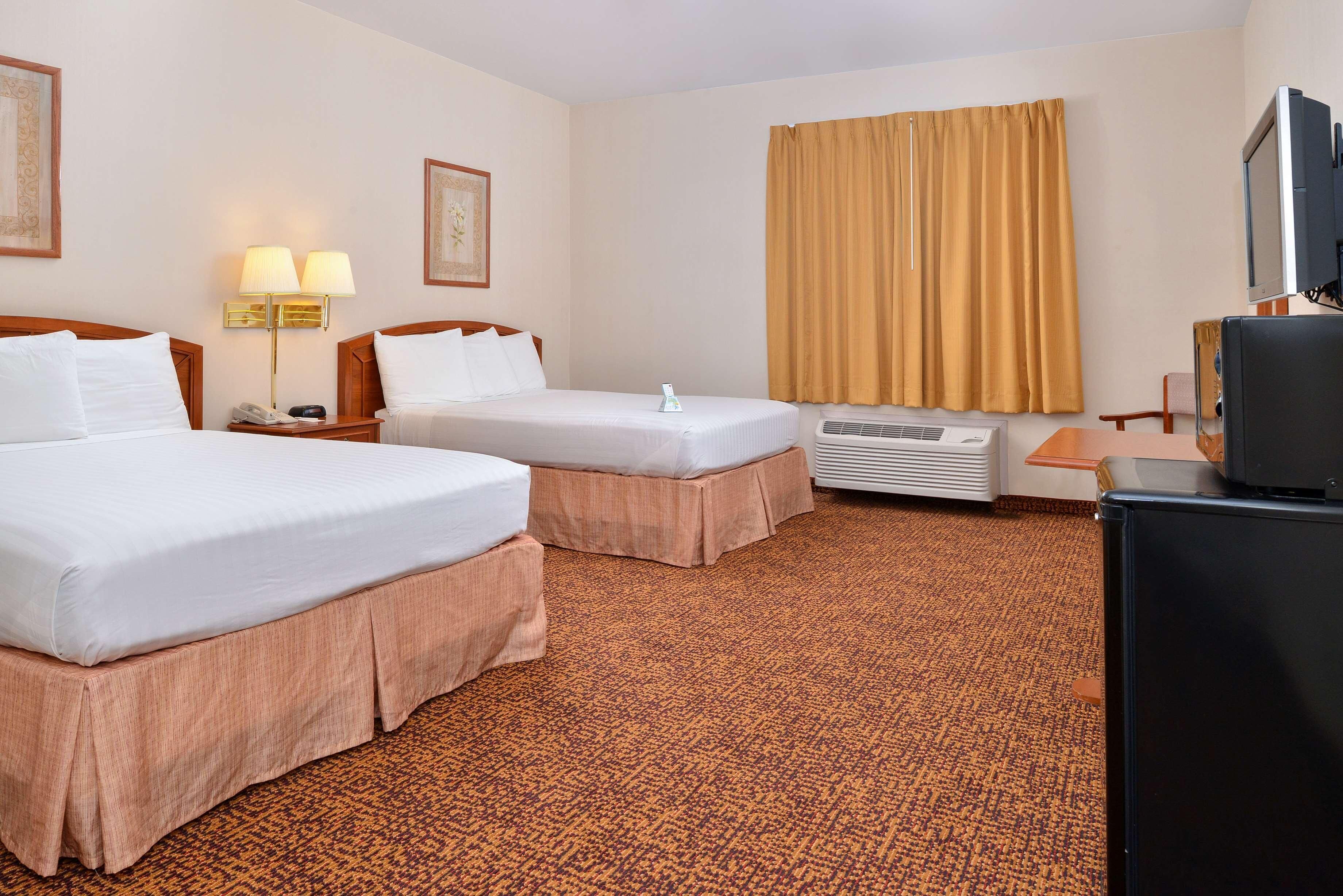 A hotel room with two beds, a desk, a television, and an air conditioning unit.