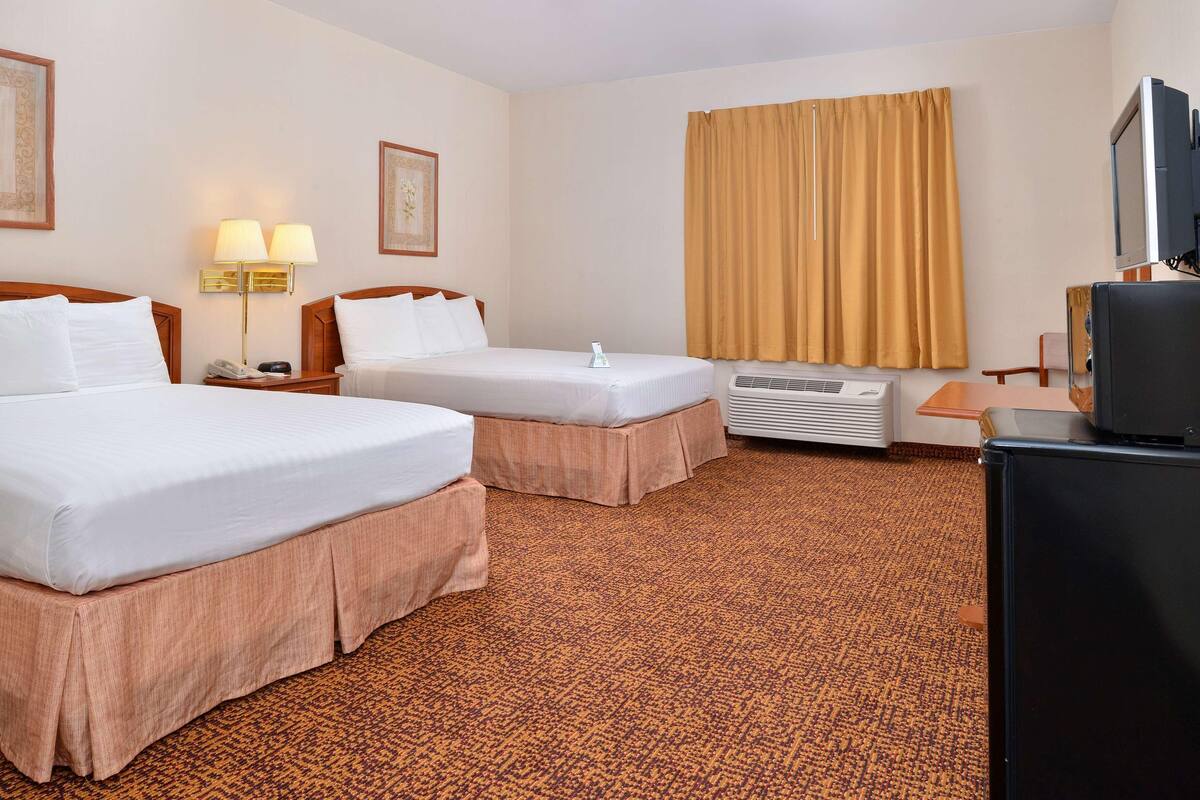 Une chambre d’hôtel avec deux lits, un bureau, une télévision et un appareil de climatisation.