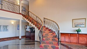 Una maestosa scalinata con ringhiere in metallo finemente decorate e un tappeto a motivi, che conduce a un piano superiore.