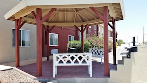 A covered outdoor seating area with a pergola structure, a white bench, and a small table.