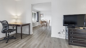 Un salon moderne doté d’un téléviseur à écran plat, d’un coin repas avec des chaises en bois, d’un bureau avec une chaise et d’une lampe.