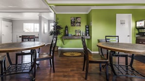 Un espace repas comprenant deux tables rondes, des chaises en bois et un mur d’accent de couleur verte.
