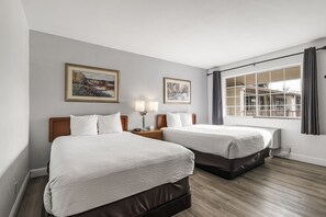 Habitación de hotel con dos camas, una ventana con cortinas y dos cuadros enmarcados en la pared.