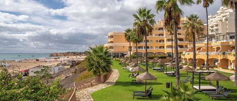 Un resort con vista a la playa, palmeras y áreas de descanso con sombrillas.