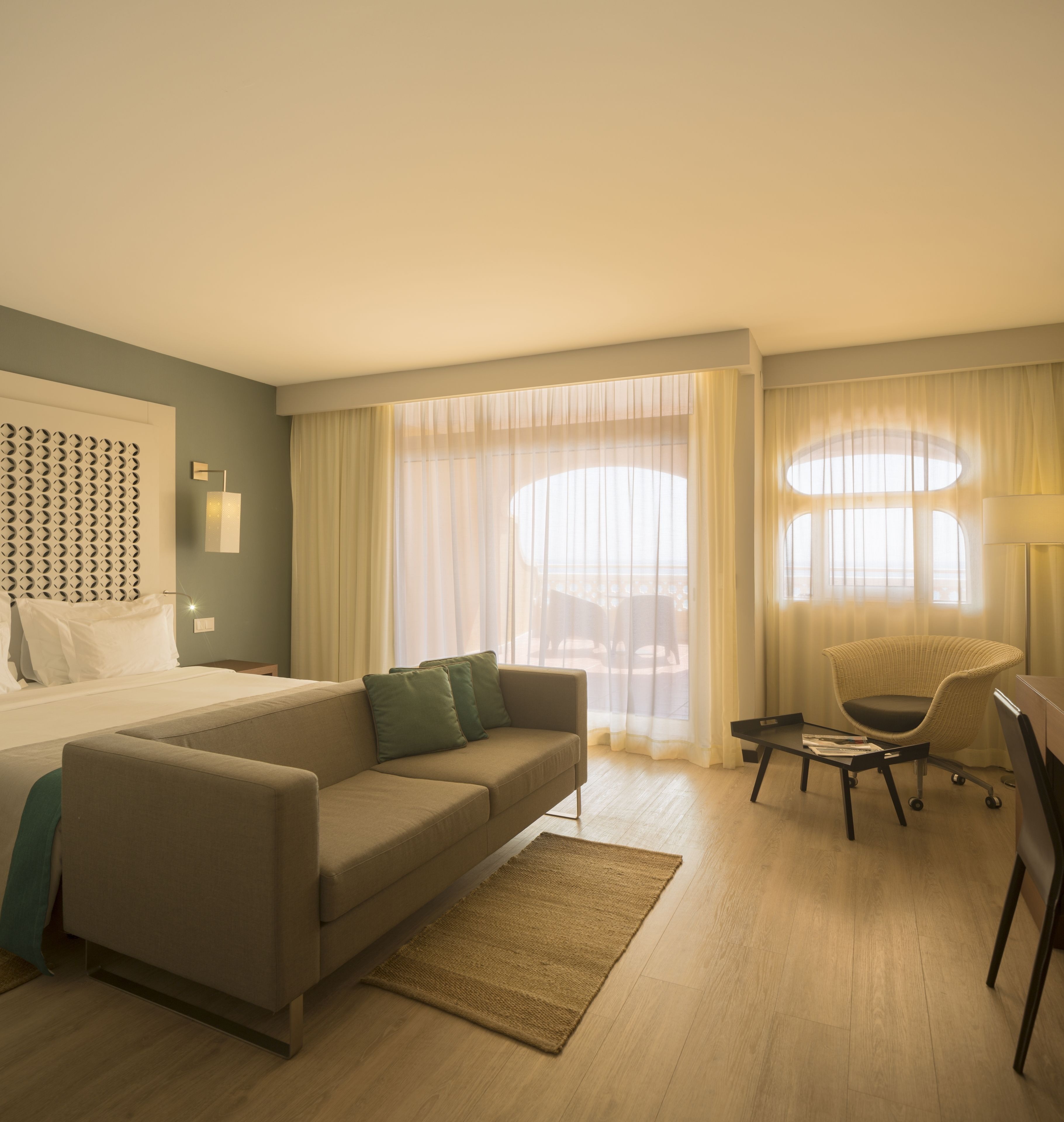 Habitación de hotel con cama, sofá, silla, una mesita y ventana con cortinas.