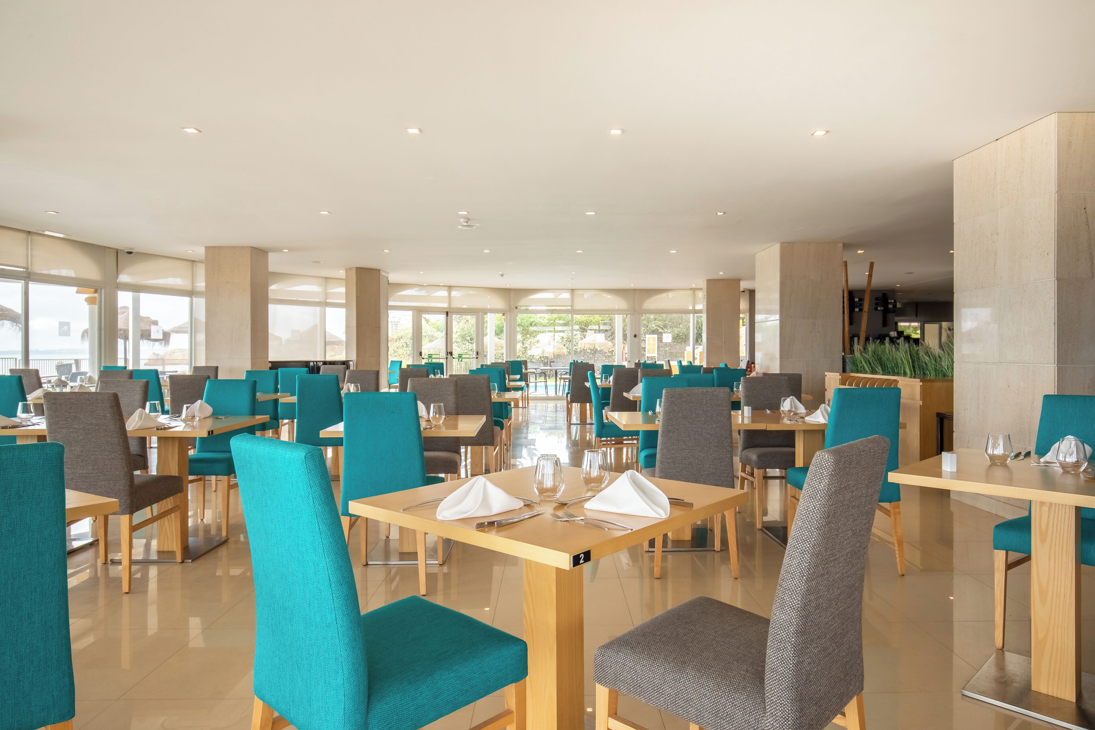 A spacious dining area with multiple tables and chairs, large windows, and a clean, modern design.