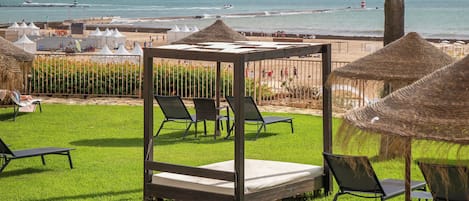 A beachside lounge area with a wooden deck, lounge chairs, and a small stage with a mattress.