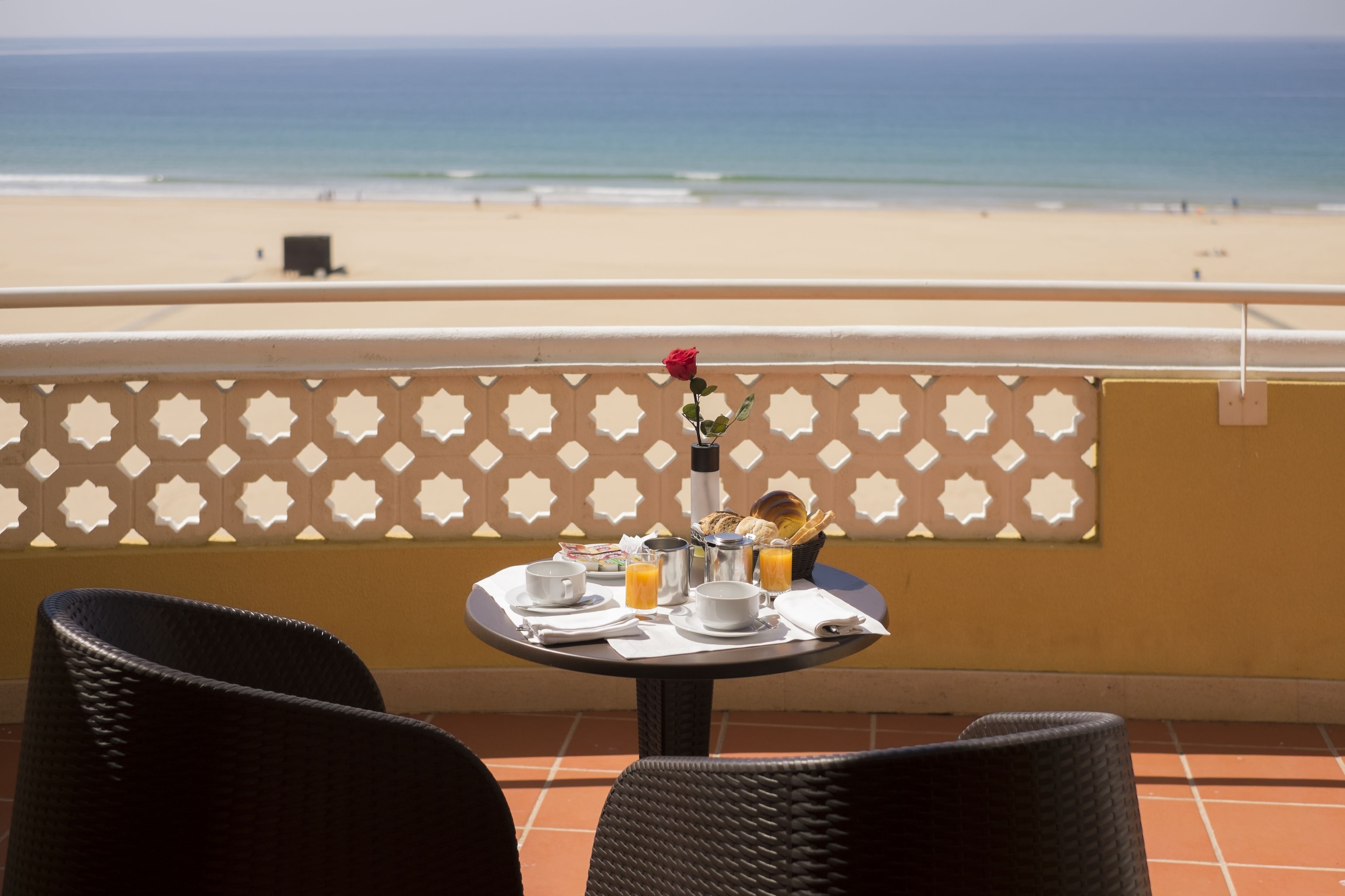 A balcony with a table set for breakfast, overlooking a beach.