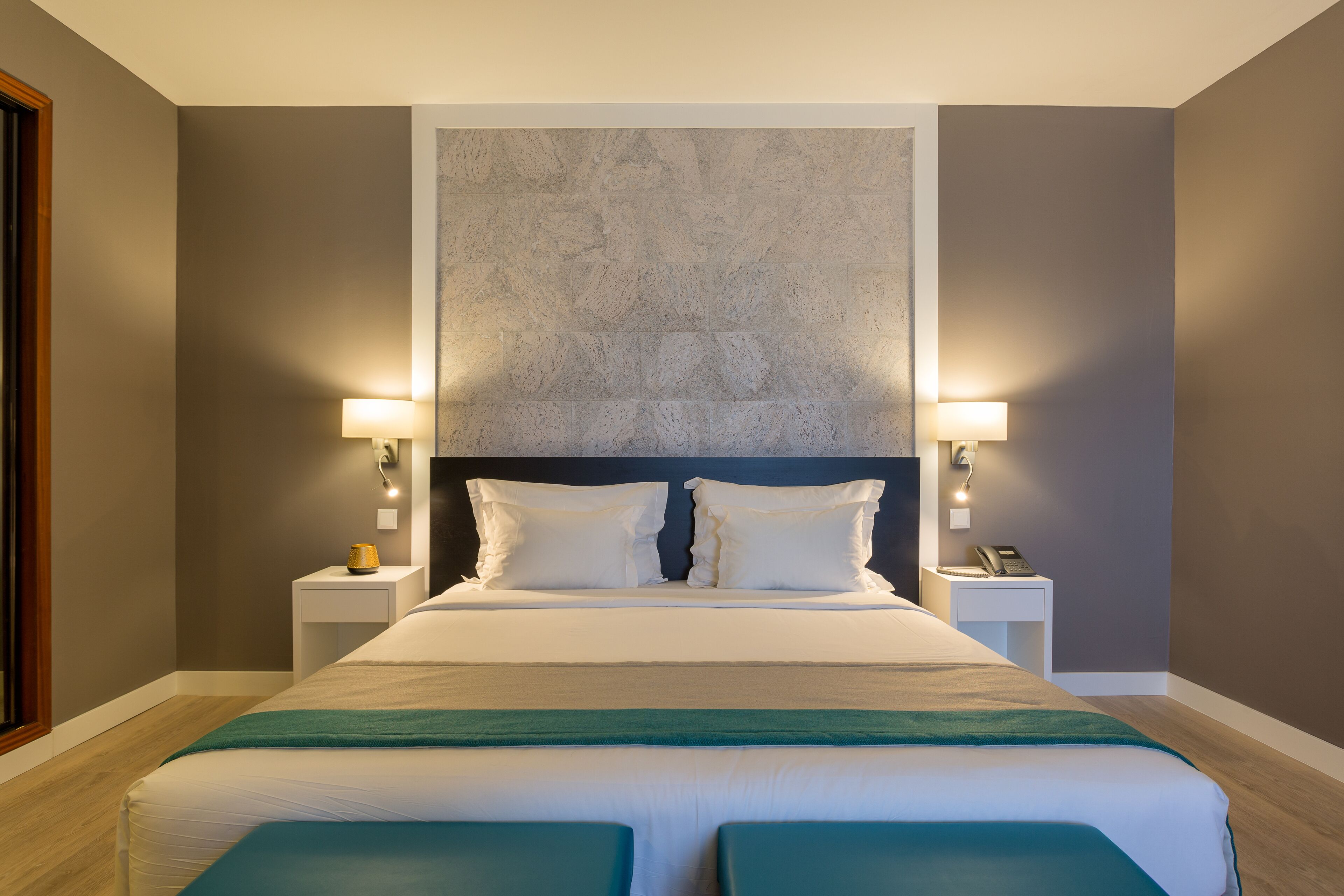 A modern hotel room with a large bed, two bedside tables with lamps, and a textured wall above the bed.