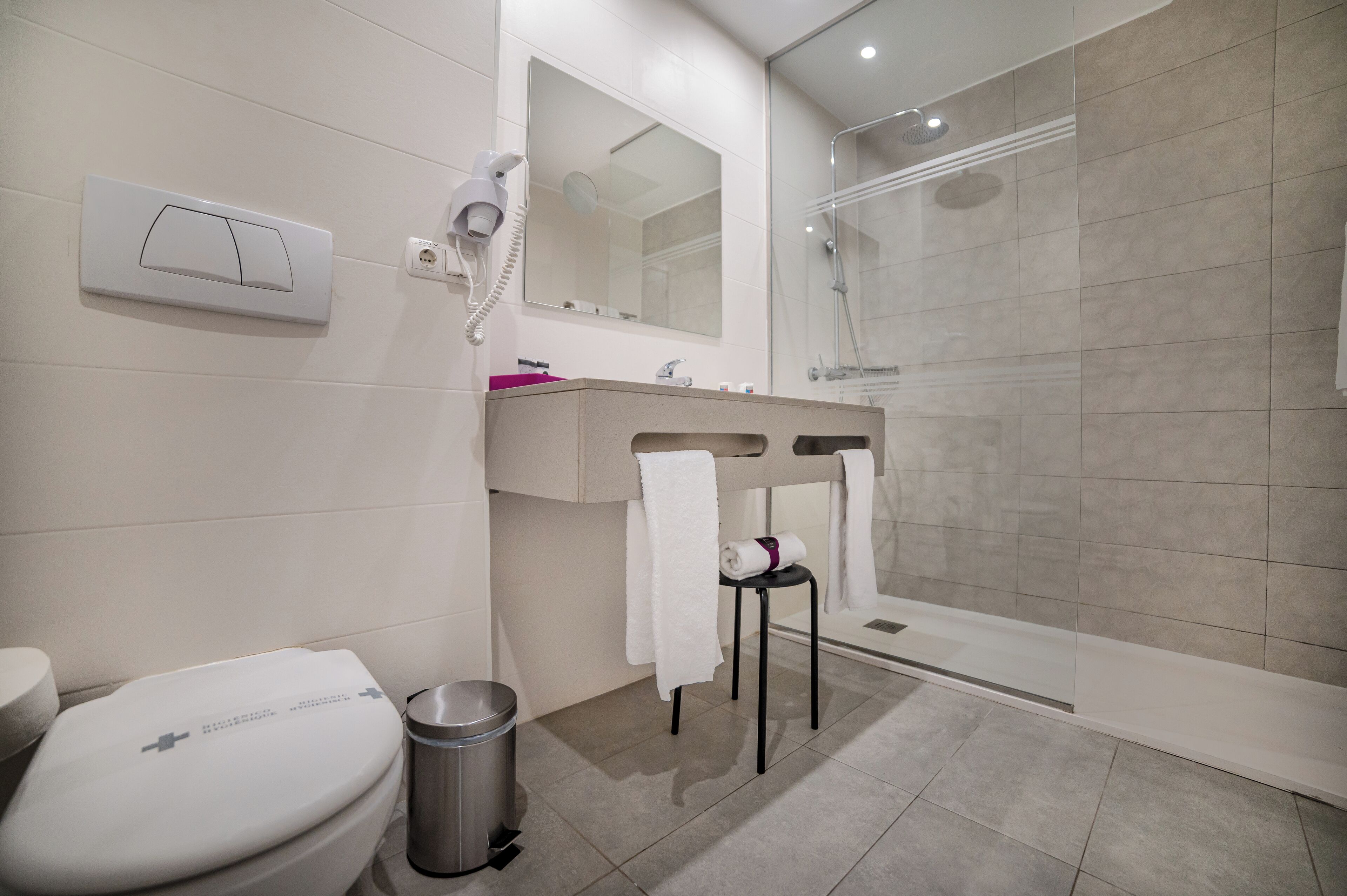 Une salle de bain moderne équipée d’un WC, d’un lavabo, d’un miroir, d’un sèche-cheveux et d’une douche.