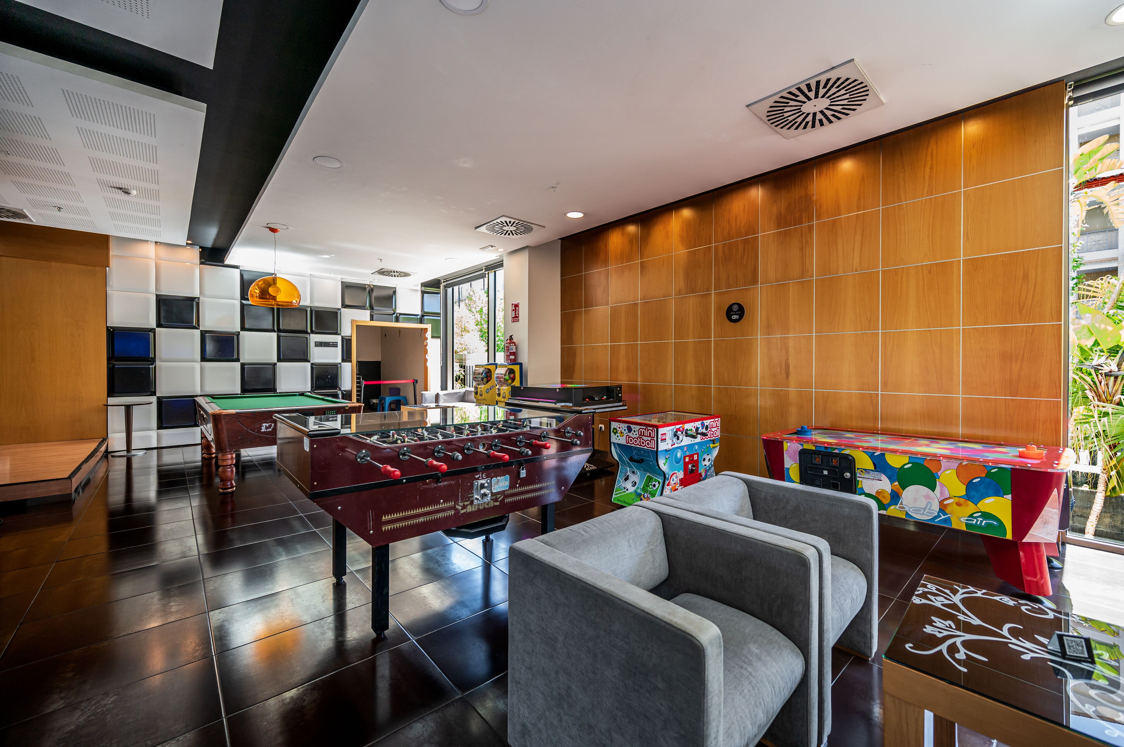Un área recreativa moderna en interiores con mesa de fútbol de mesa, mesa de billar y una mesa de tenis de mesa colorida.