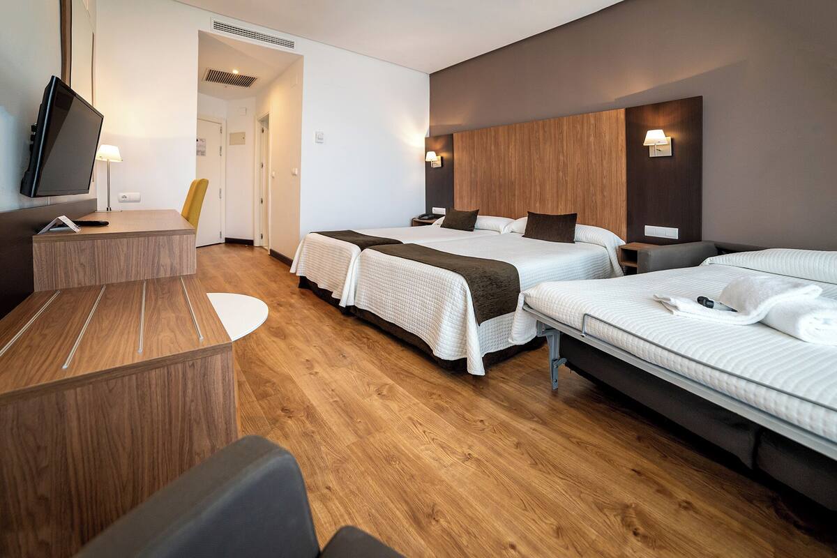 A hotel room with two beds, a desk, a chair, and a TV.