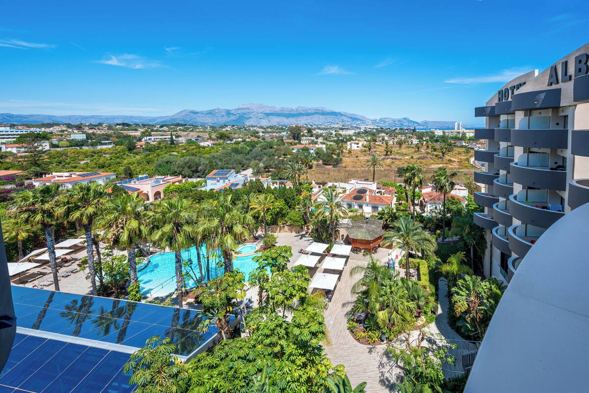 A hotel with a pool, palm trees, and a view of mountains.
