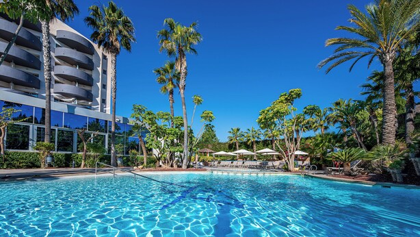 A clear blue pool surrounded by palm trees and a modern building with balconies. - Albir Playa Hotel & Spa (L'Alfas del Pi)