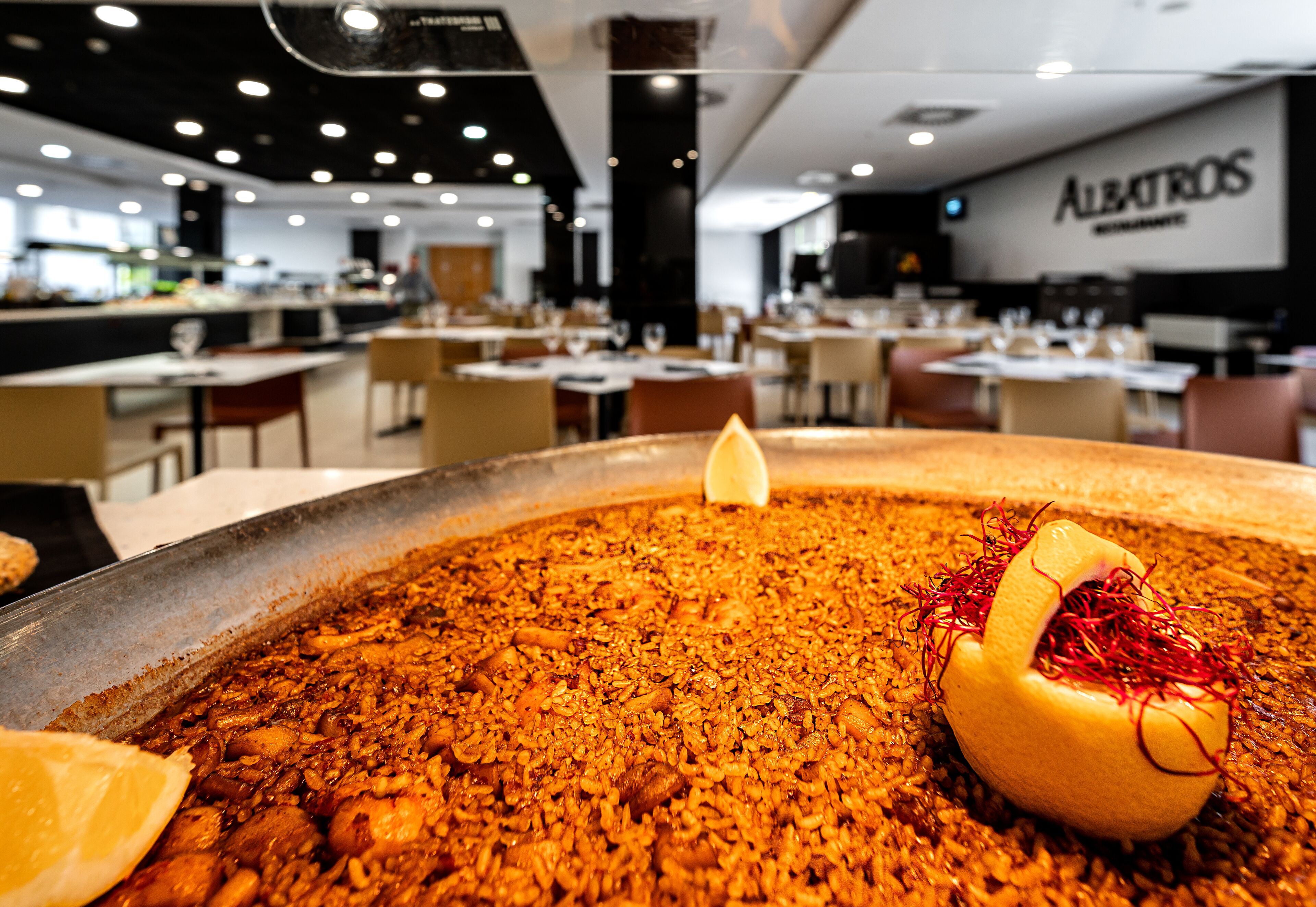 Una amplia mesa común para comer, con un plato de arroz y carne, rodeada de sillas en un restaurante.