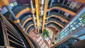 A multi-level atrium with a central elevator shaft, glass railings, and a landscaped area with rocks and plants. - Albir Playa Hotel & Spa (L'Alfas del Pi)