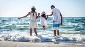 Una familia de tres caminando por la playa mientras las olas rompen a su alrededor.