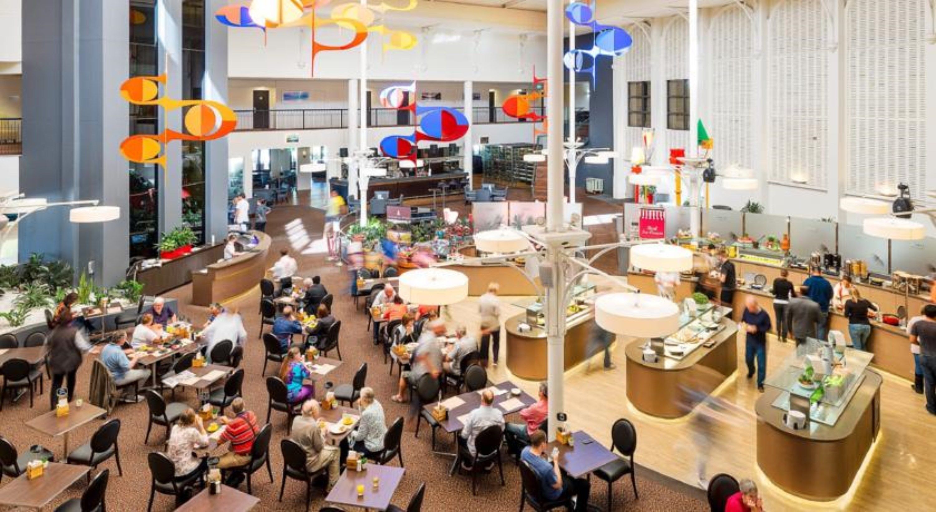 A spacious indoor dining area with multiple tables and chairs, a central serving counter, and hanging decorative elements.