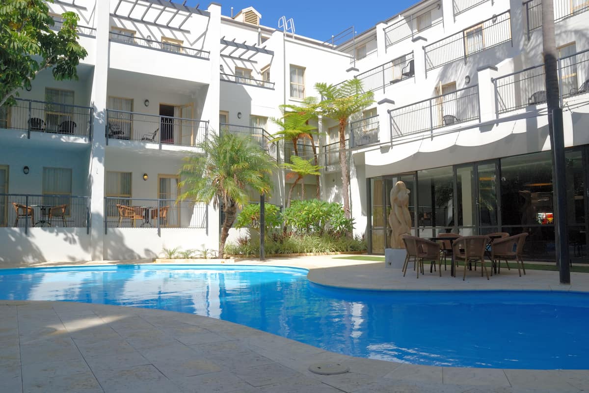 A pool area with a clear blue pool, surrounded by a white building with balconies and outdoor seating.