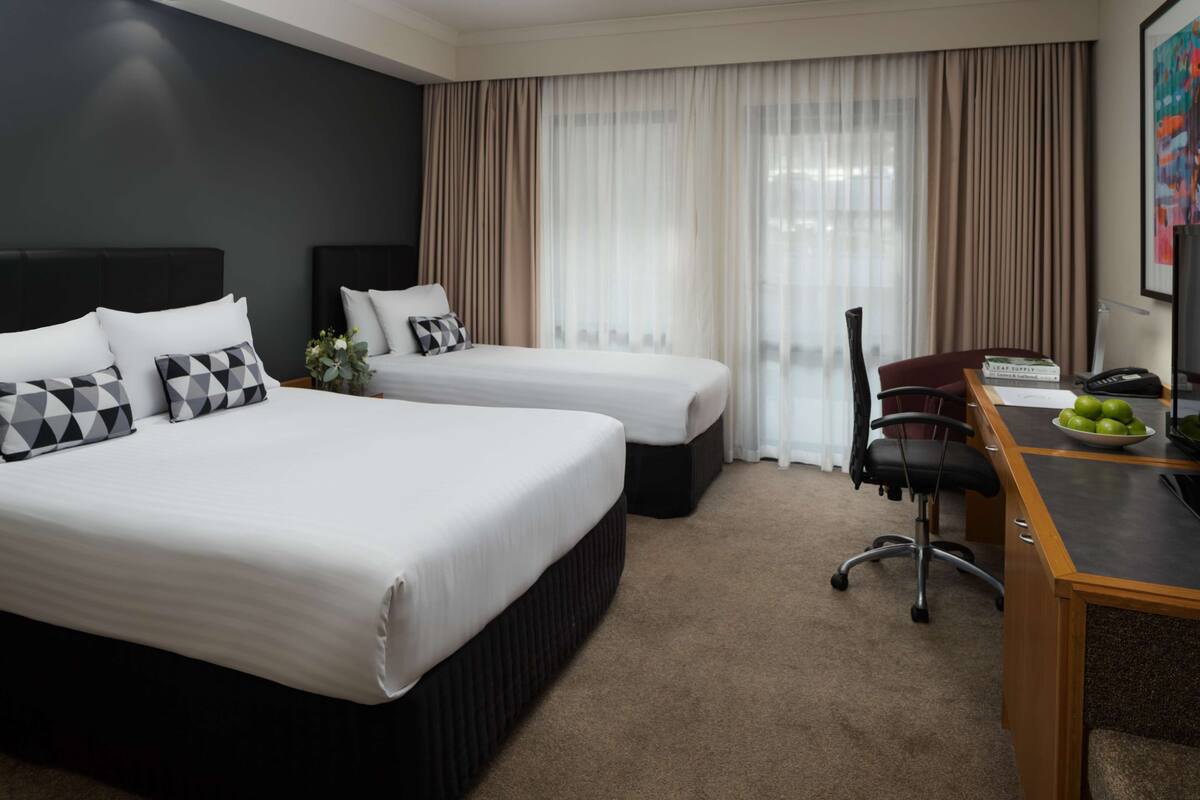 A hotel room with two beds, a desk, a chair, and a TV.