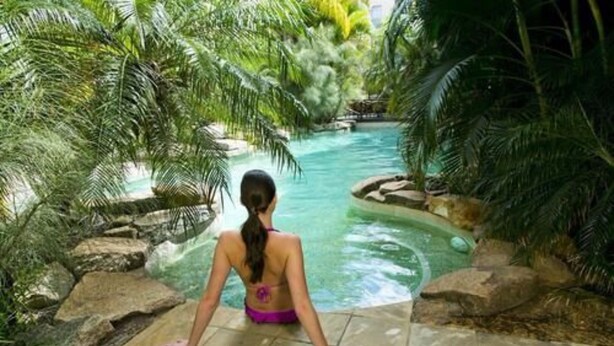 Una mujer sentada junto a una piscina rodeada de follaje tropical.