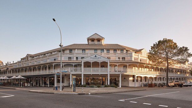A large, multi-story hotel with a prominent Esplanade Hotel sign. It features a central atrium with balconies, multiple levels of shops, and outdoor seating areas.