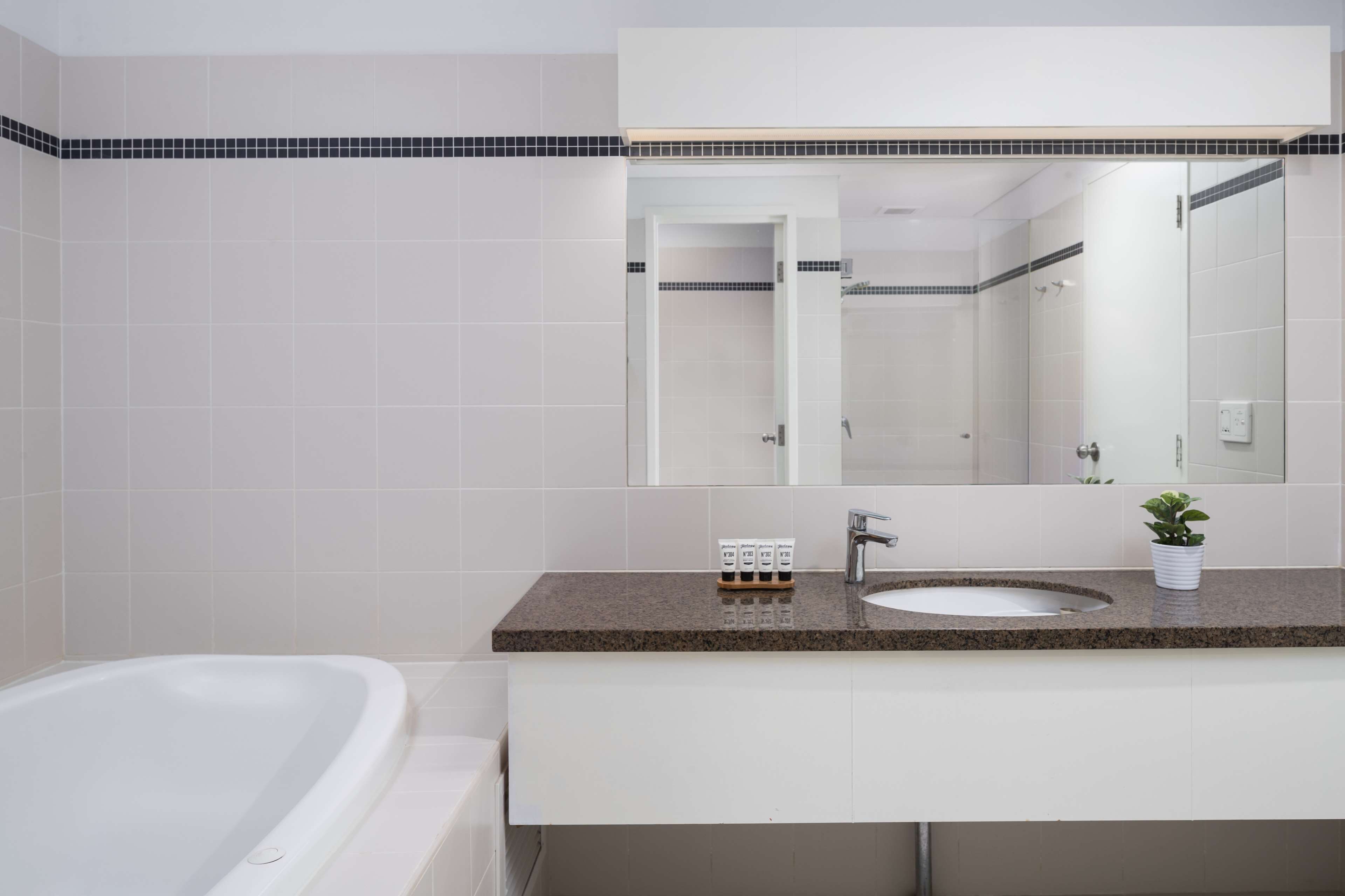 A modern bathroom with a white bathtub, a sink with a granite countertop, and a large mirror above the sink.