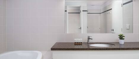 A modern bathroom with a white bathtub, a sink with a granite countertop, and a large mirror above the sink.