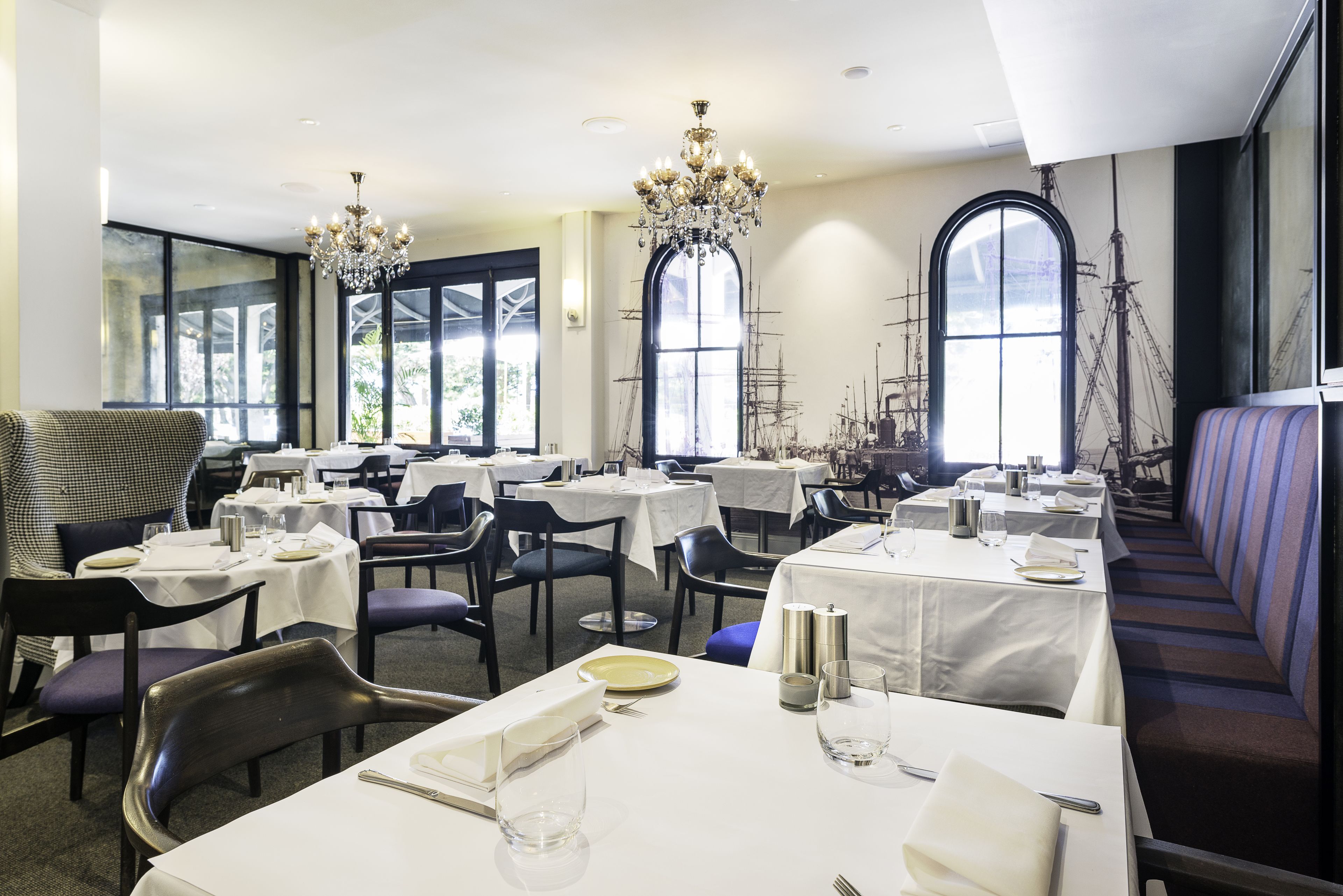 A dining area with tables set for service, large windows, and a chandelier.