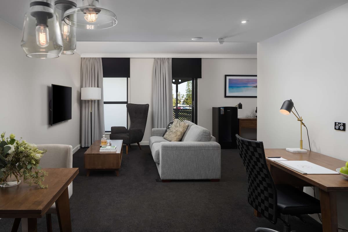 A modern living room with a grey sofa, a wooden coffee table, a black armchair, and a desk with a lamp.