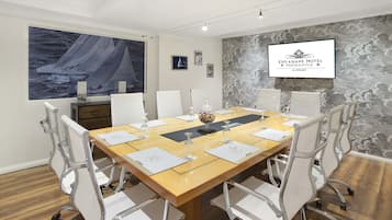 Un salón de conferencias con una mesa de madera, sillas blancas y un cuadro grande de un velero en la pared.