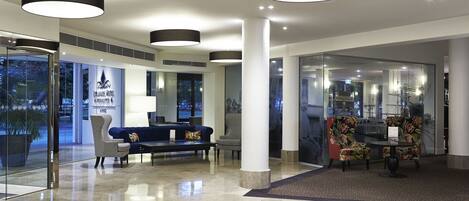 A modern lobby with a reception desk, seating area, and large windows.