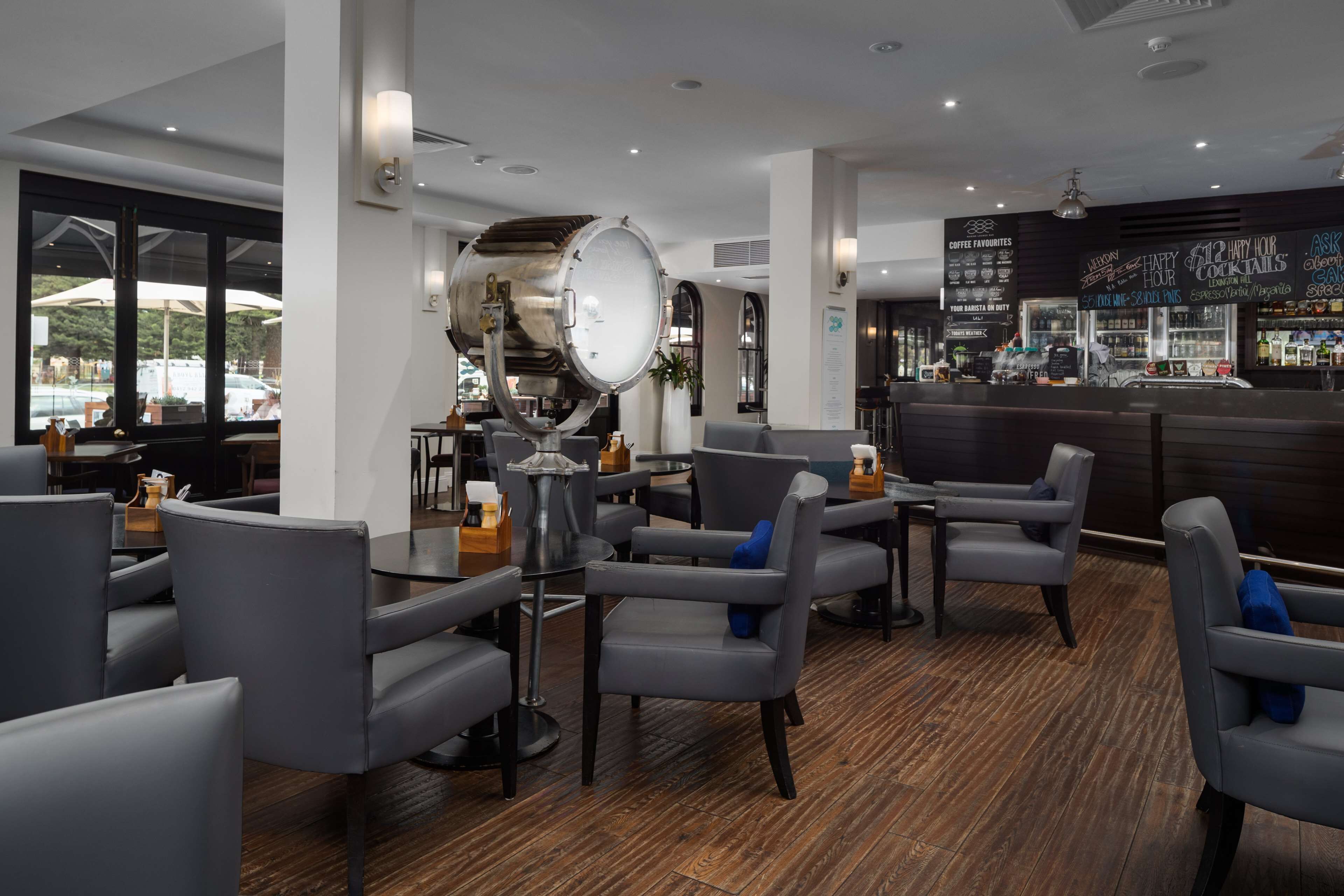 Un espace bar moderne avec des sièges, un grand tonneau en métal et un tableau affichant le menu.