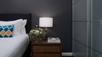 A neatly made bed with a patterned pillow, a bedside table with a lamp, a vase with flowers, and a book titled "Leaf Supply".