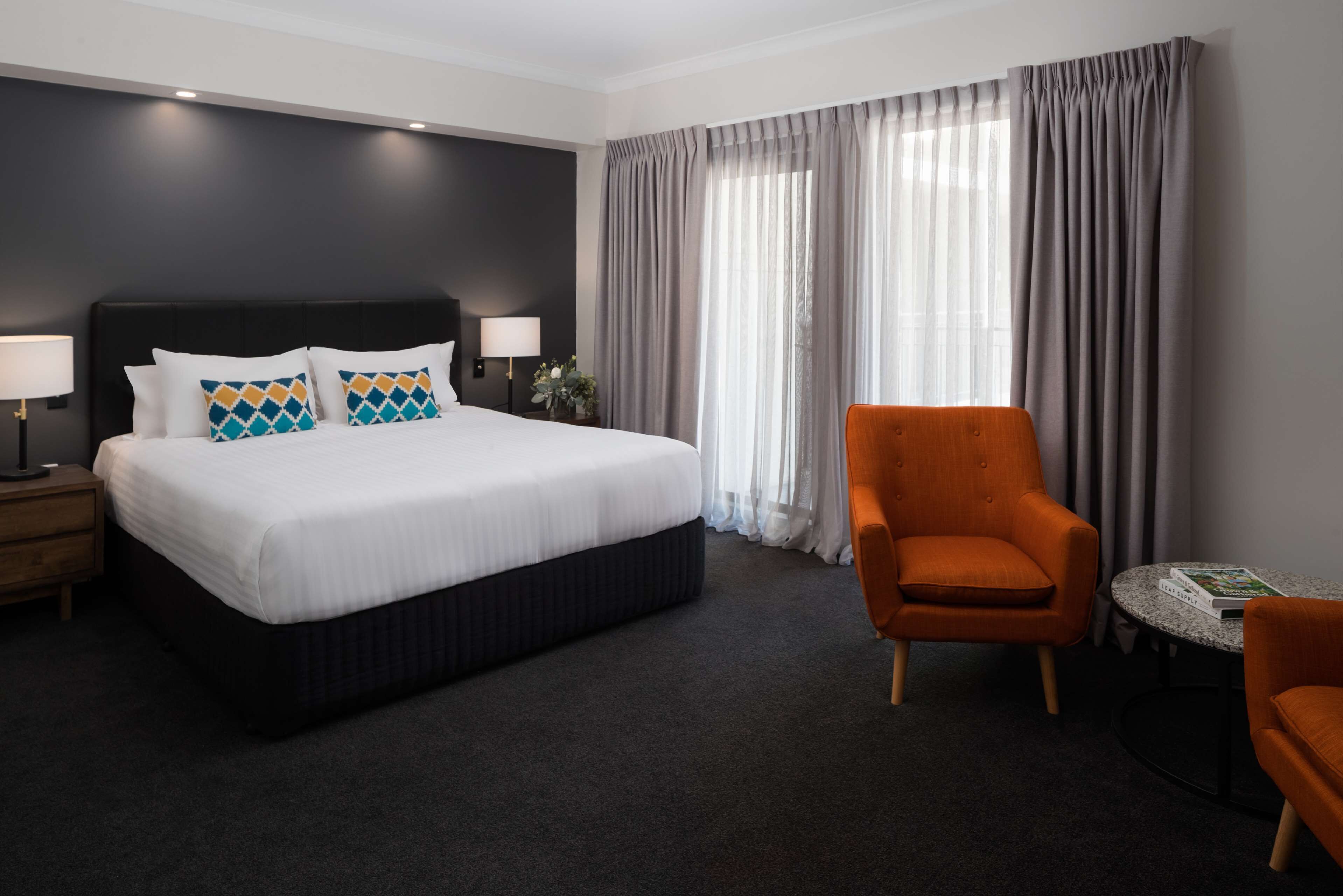 Une chambre d’hôtel avec un grand lit, une table de chevet avec une lampe, une chaise et une petite table avec un livre.